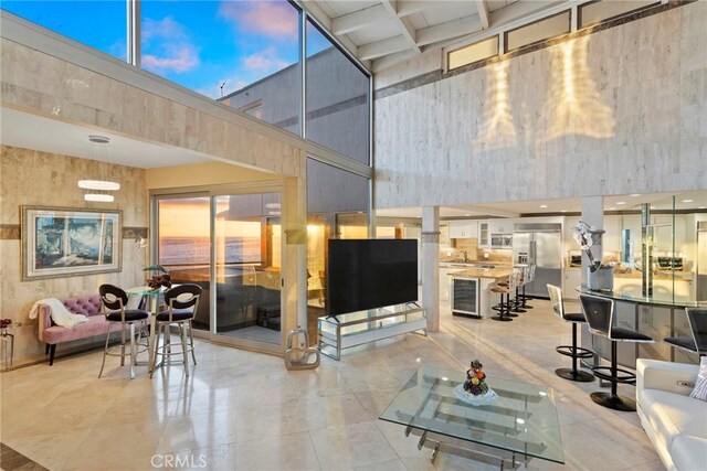 living room with wine cooler, a towering ceiling, and beamed ceiling