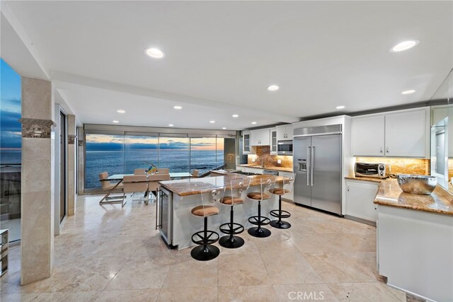 kitchen featuring light stone countertops, built in appliances, and white cabinets