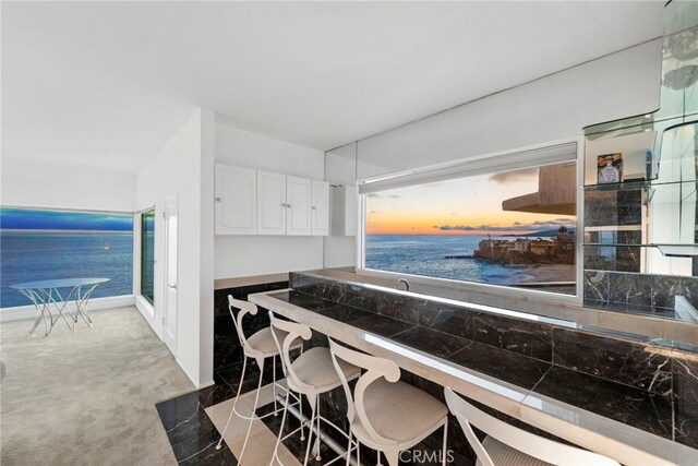 kitchen featuring white cabinetry, a kitchen bar, light colored carpet, and a water view