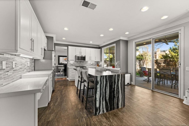 kitchen featuring dark wood-type flooring, white cabinetry, a kitchen breakfast bar, a kitchen island, and backsplash