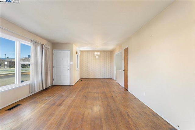 spare room with hardwood / wood-style floors, a wealth of natural light, and a notable chandelier