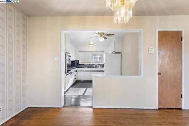 kitchen featuring dark wood-type flooring, white cabinetry, ceiling fan with notable chandelier, white refrigerator, and sink