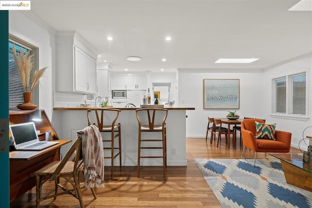 kitchen featuring stainless steel microwave, backsplash, kitchen peninsula, a kitchen bar, and white cabinets