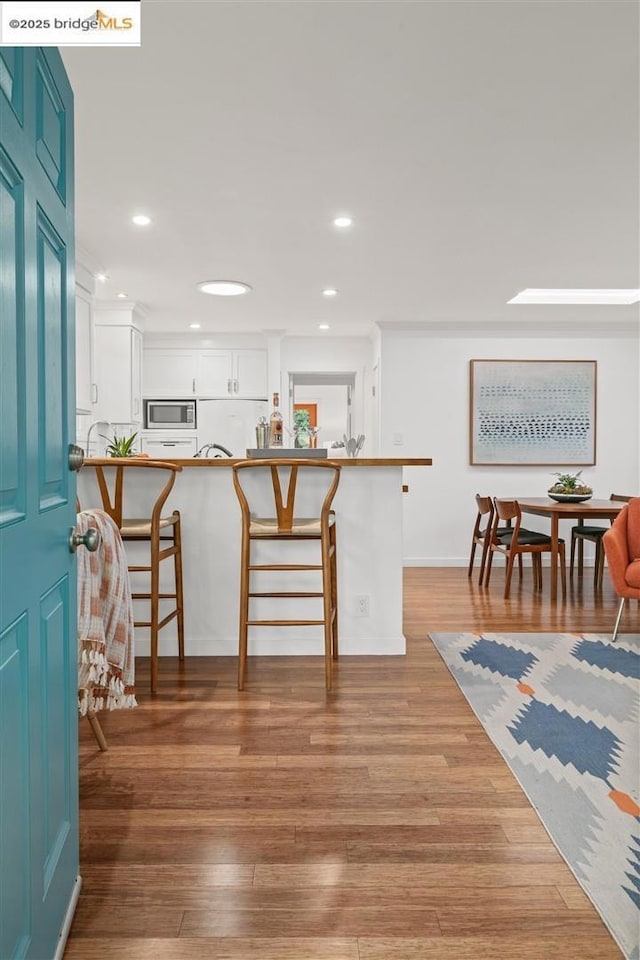 kitchen with stainless steel microwave, white cabinets, kitchen peninsula, and a kitchen breakfast bar