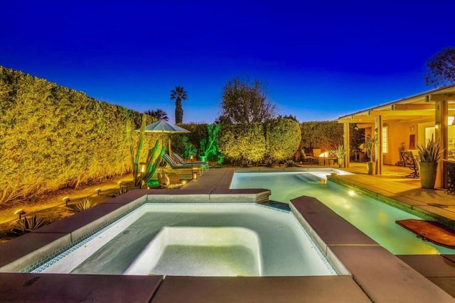 pool at dusk with an in ground hot tub and a patio area