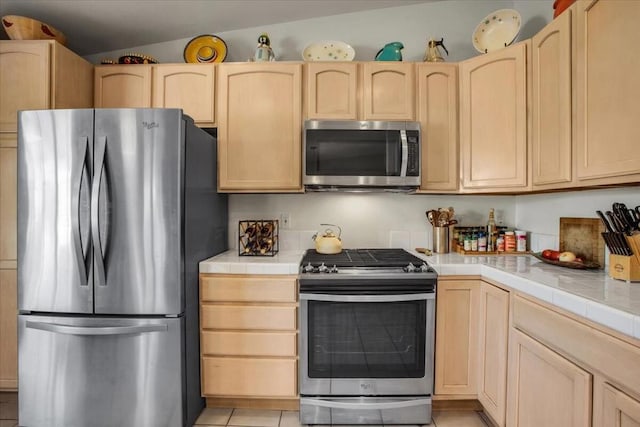 kitchen featuring stainless steel appliances, vaulted ceiling, tile countertops, and light brown cabinets