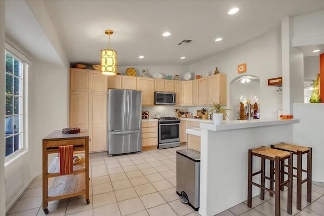 kitchen with light tile patterned floors, appliances with stainless steel finishes, hanging light fixtures, kitchen peninsula, and light brown cabinets