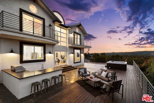 deck at dusk with an outdoor wet bar, a hot tub, and an outdoor hangout area