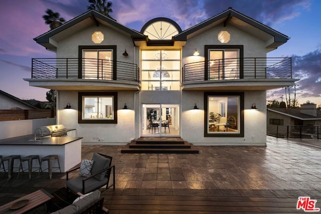 back house at dusk featuring a balcony, a patio, and a wet bar