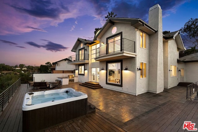 back house at dusk featuring a balcony, a hot tub, and a patio