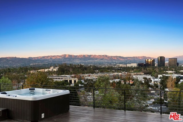 deck at dusk with a hot tub and a mountain view