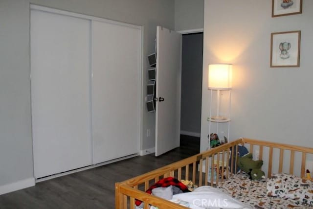 bedroom with a closet, dark hardwood / wood-style floors, and a crib