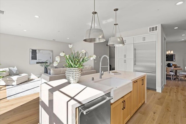 kitchen with stainless steel appliances, sink, white cabinets, light wood-type flooring, and pendant lighting