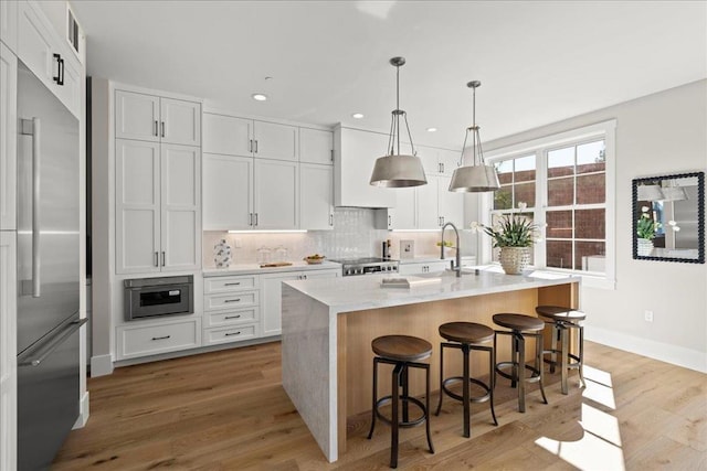 kitchen with stainless steel built in refrigerator, white cabinetry, and a kitchen island with sink