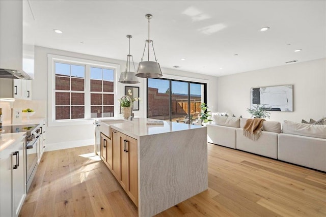 kitchen featuring range hood, high end range, an island with sink, light hardwood / wood-style floors, and white cabinets