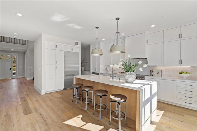 kitchen with stainless steel built in refrigerator, white cabinetry, a kitchen breakfast bar, an island with sink, and pendant lighting