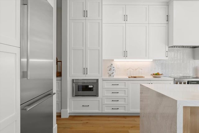 kitchen with range, stainless steel refrigerator, light wood-type flooring, white cabinets, and backsplash