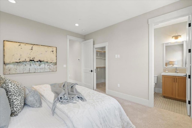 bedroom with a spacious closet, light carpet, a closet, and ensuite bath