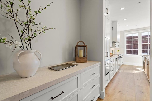 interior space with oven, light hardwood / wood-style flooring, and white cabinetry