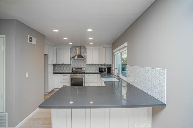 kitchen featuring white cabinets, wall chimney range hood, kitchen peninsula, and appliances with stainless steel finishes