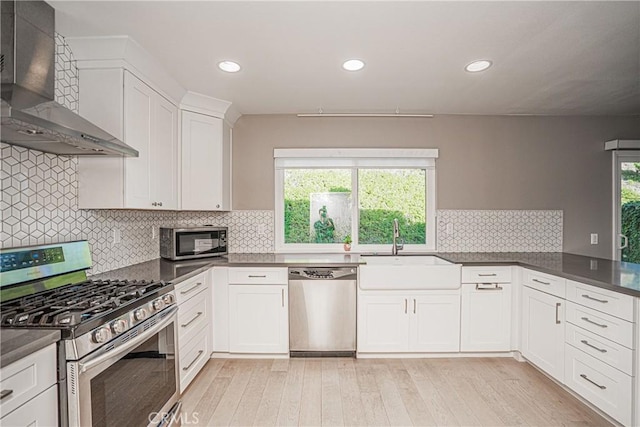 kitchen featuring appliances with stainless steel finishes, light hardwood / wood-style floors, sink, white cabinetry, and wall chimney range hood