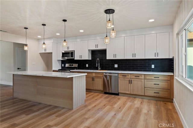 kitchen featuring white cabinetry, appliances with stainless steel finishes, decorative light fixtures, and a center island