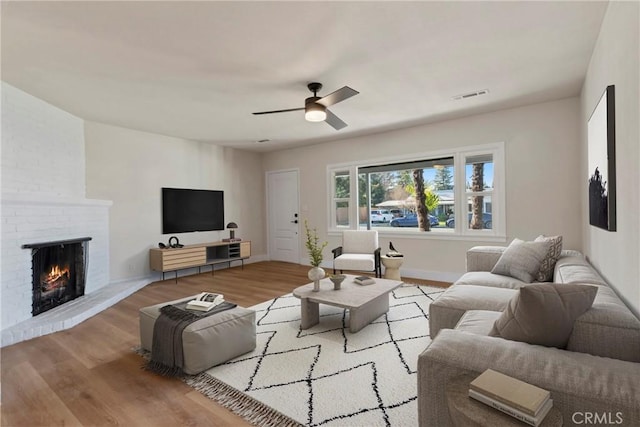 living room featuring ceiling fan, a brick fireplace, and light wood-type flooring