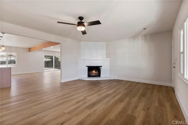 unfurnished living room with a brick fireplace, beam ceiling, hardwood / wood-style floors, and ceiling fan