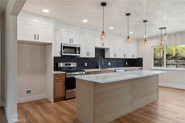 kitchen featuring white cabinets, hanging light fixtures, a center island, stainless steel appliances, and light stone countertops