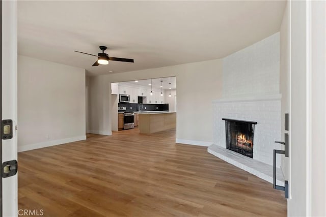 unfurnished living room with ceiling fan, light hardwood / wood-style floors, sink, and a brick fireplace