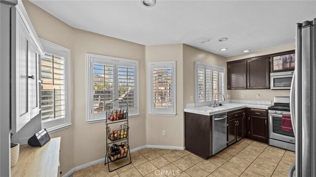 kitchen with stainless steel appliances, sink, light tile patterned floors, and dark brown cabinetry