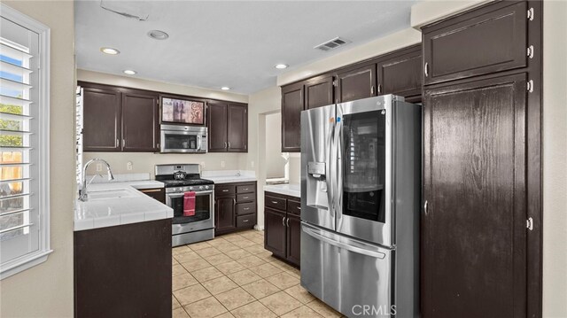 kitchen with appliances with stainless steel finishes, light tile patterned floors, sink, and dark brown cabinetry