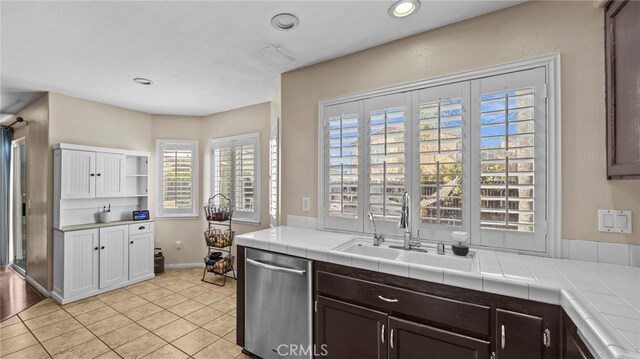 kitchen featuring light tile patterned floors, tile countertops, sink, dark brown cabinets, and stainless steel dishwasher