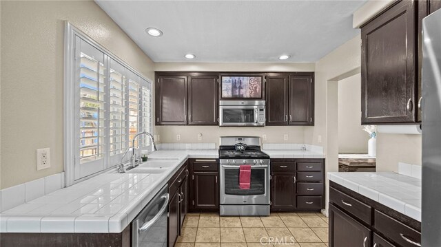 kitchen featuring appliances with stainless steel finishes, light tile patterned floors, tile countertops, sink, and dark brown cabinets