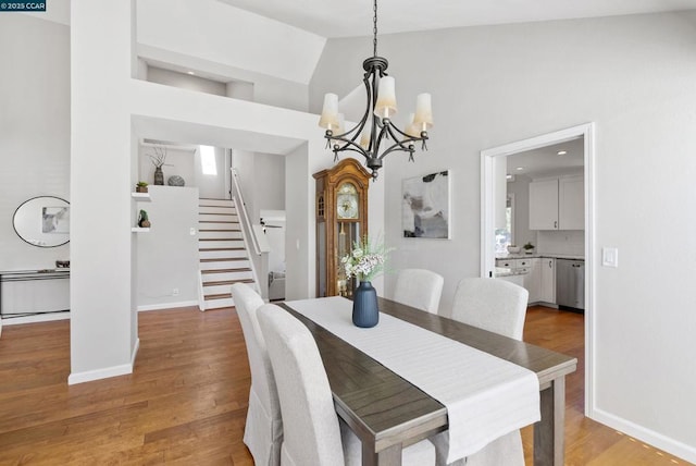 dining space featuring a notable chandelier, light wood-type flooring, and high vaulted ceiling