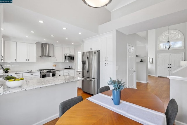 kitchen featuring stainless steel appliances, light stone countertops, wall chimney exhaust hood, white cabinetry, and decorative light fixtures