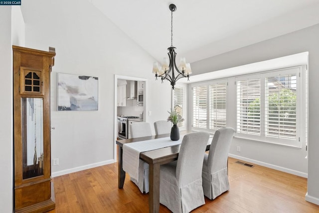 dining space with light hardwood / wood-style flooring, high vaulted ceiling, and a chandelier