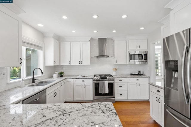 kitchen with sink, white cabinets, light hardwood / wood-style flooring, wall chimney range hood, and appliances with stainless steel finishes