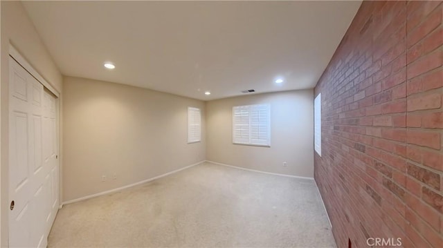 carpeted empty room featuring brick wall