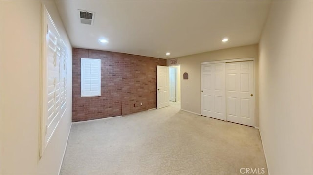 unfurnished bedroom with brick wall, a closet, and light carpet