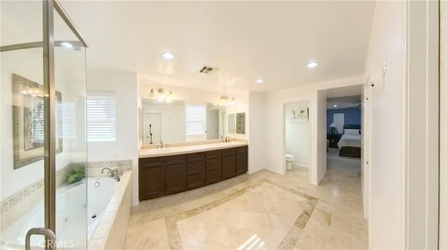 bathroom with vanity, tiled bath, and toilet