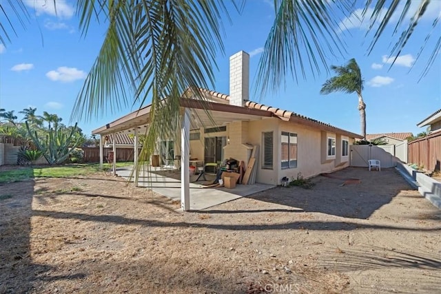 back of property featuring a tile roof, a fenced backyard, a chimney, a patio area, and stucco siding