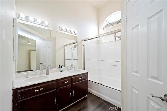 full bath featuring double vanity, wood finished floors, bath / shower combo with glass door, and a sink