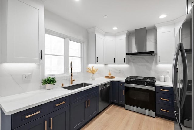 kitchen featuring gas range oven, stainless steel dishwasher, wall chimney exhaust hood, white cabinetry, and sink