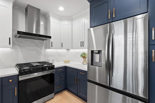 kitchen featuring white cabinets, stainless steel appliances, blue cabinetry, and wall chimney range hood