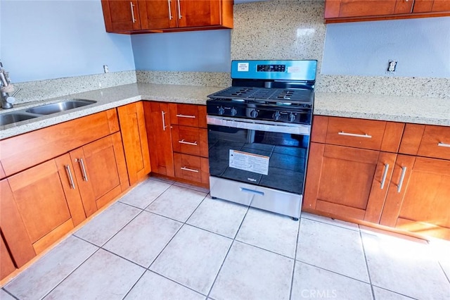 kitchen with sink, gas range, light stone countertops, and light tile patterned flooring