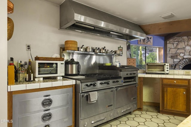 kitchen featuring tile counters, wall chimney range hood, and range with two ovens