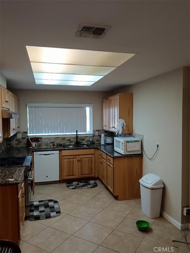 kitchen with sink, dark stone countertops, white appliances, and light tile patterned floors