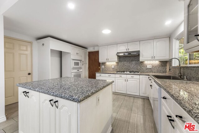 kitchen featuring white cabinetry, sink, dark stone countertops, a center island, and white appliances