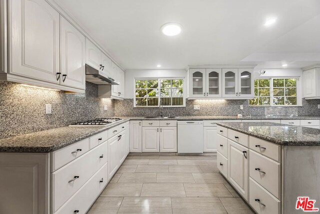 kitchen featuring stainless steel gas stovetop, white cabinetry, dishwasher, backsplash, and dark stone counters